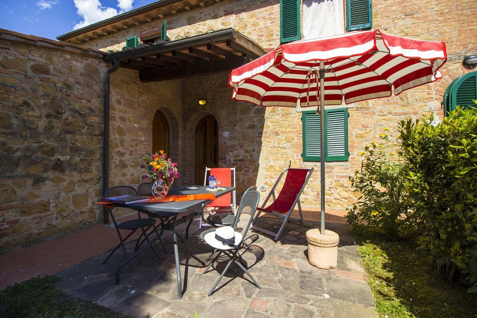 A patio with an umbrella and chairs outside of a house.