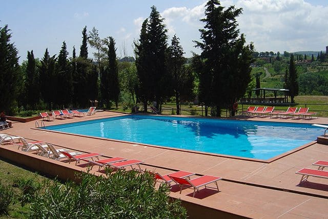 A pool with red chairs and trees in the background