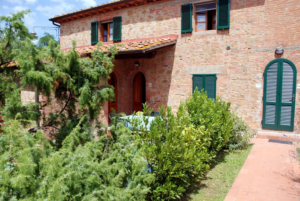 A brick house with green shutters and bushes.